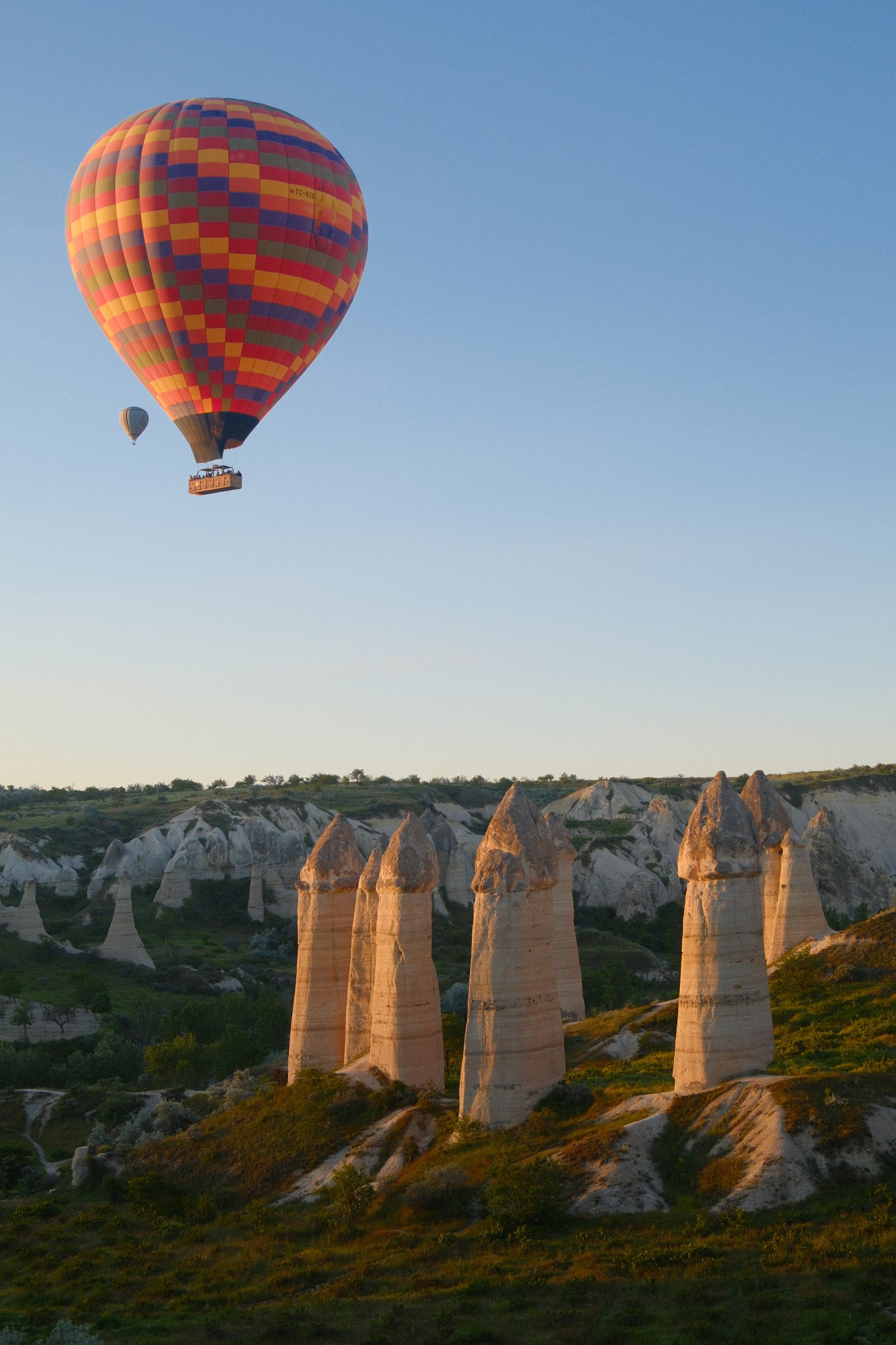 A hot air balloon over Cappadocia's fairy chimneys, another balloon rising in the distance.