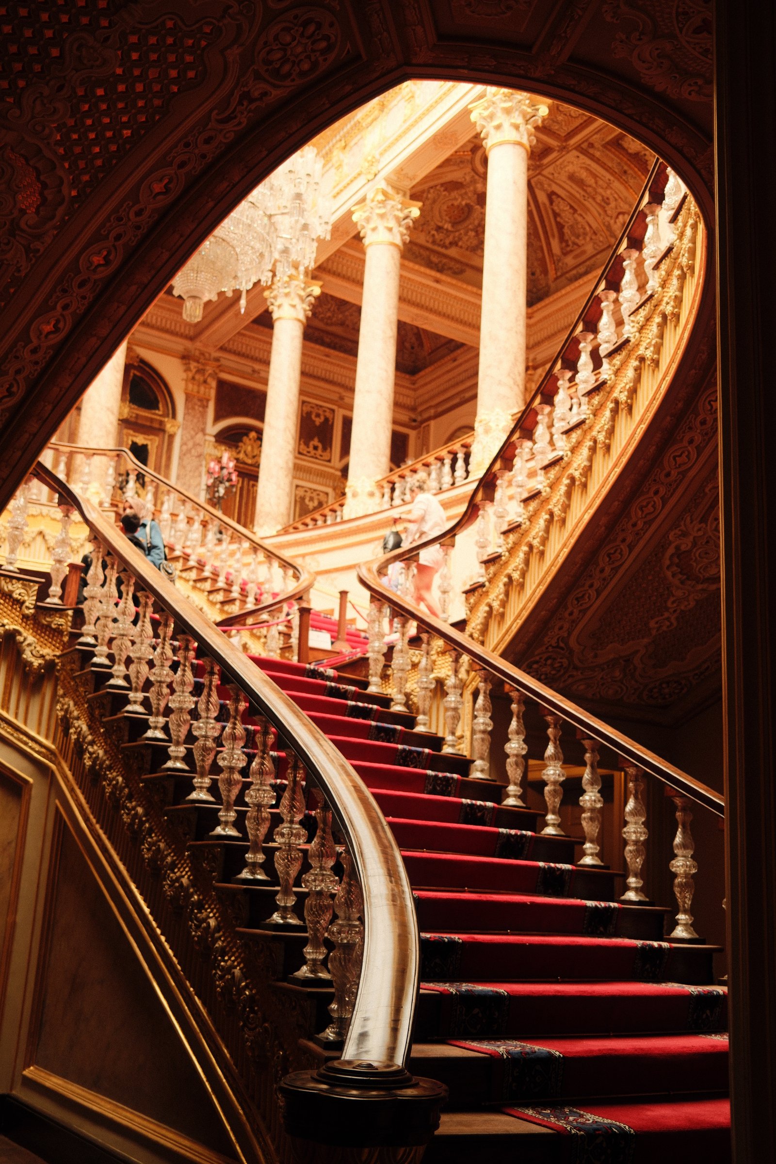 A grand crystal staircase at Dolmabahce Palace, red carpet running down gold-railed steps.