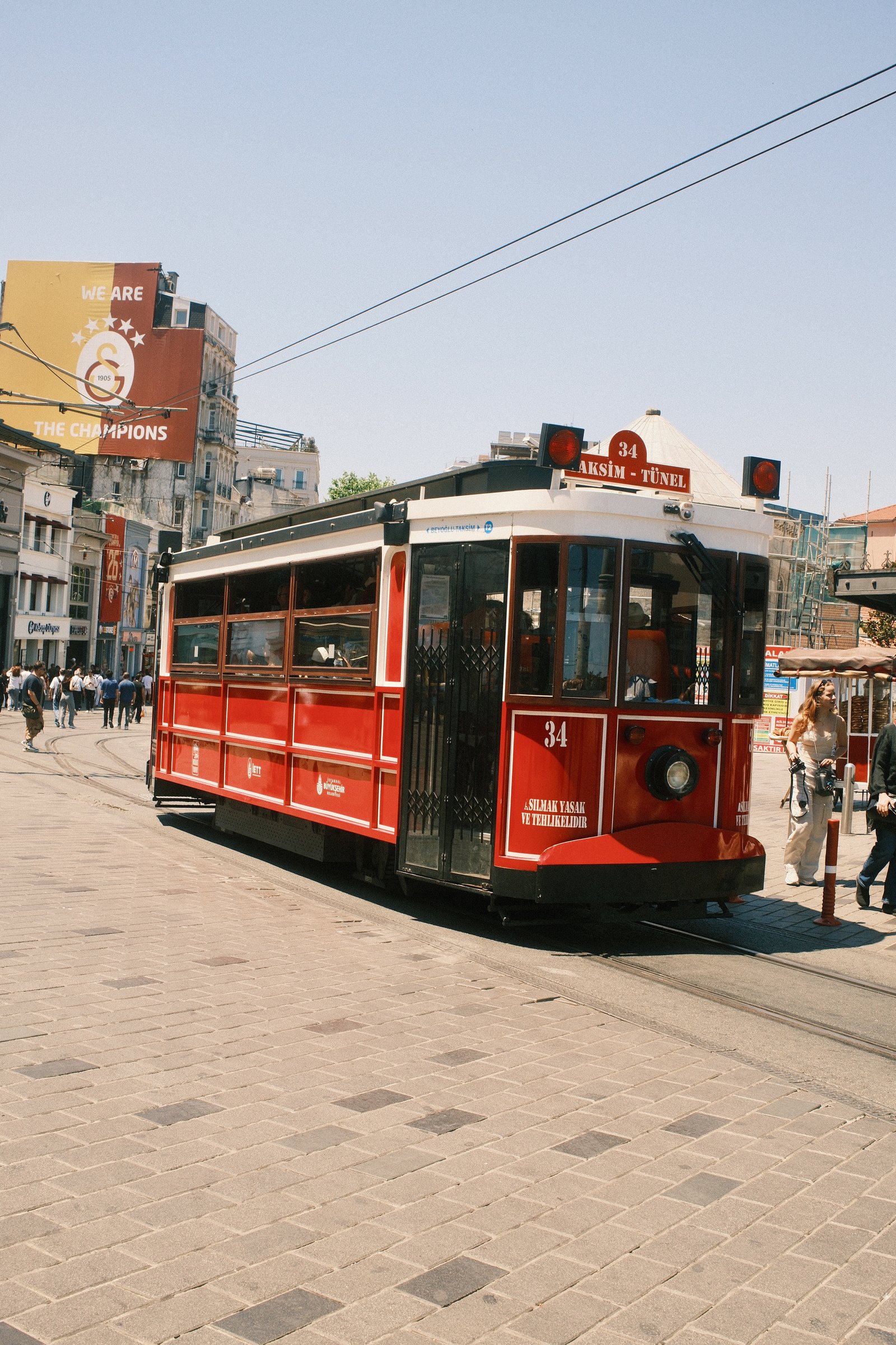A red heritage tram on Istiklal Avenue, pedestrians crossing behind it.