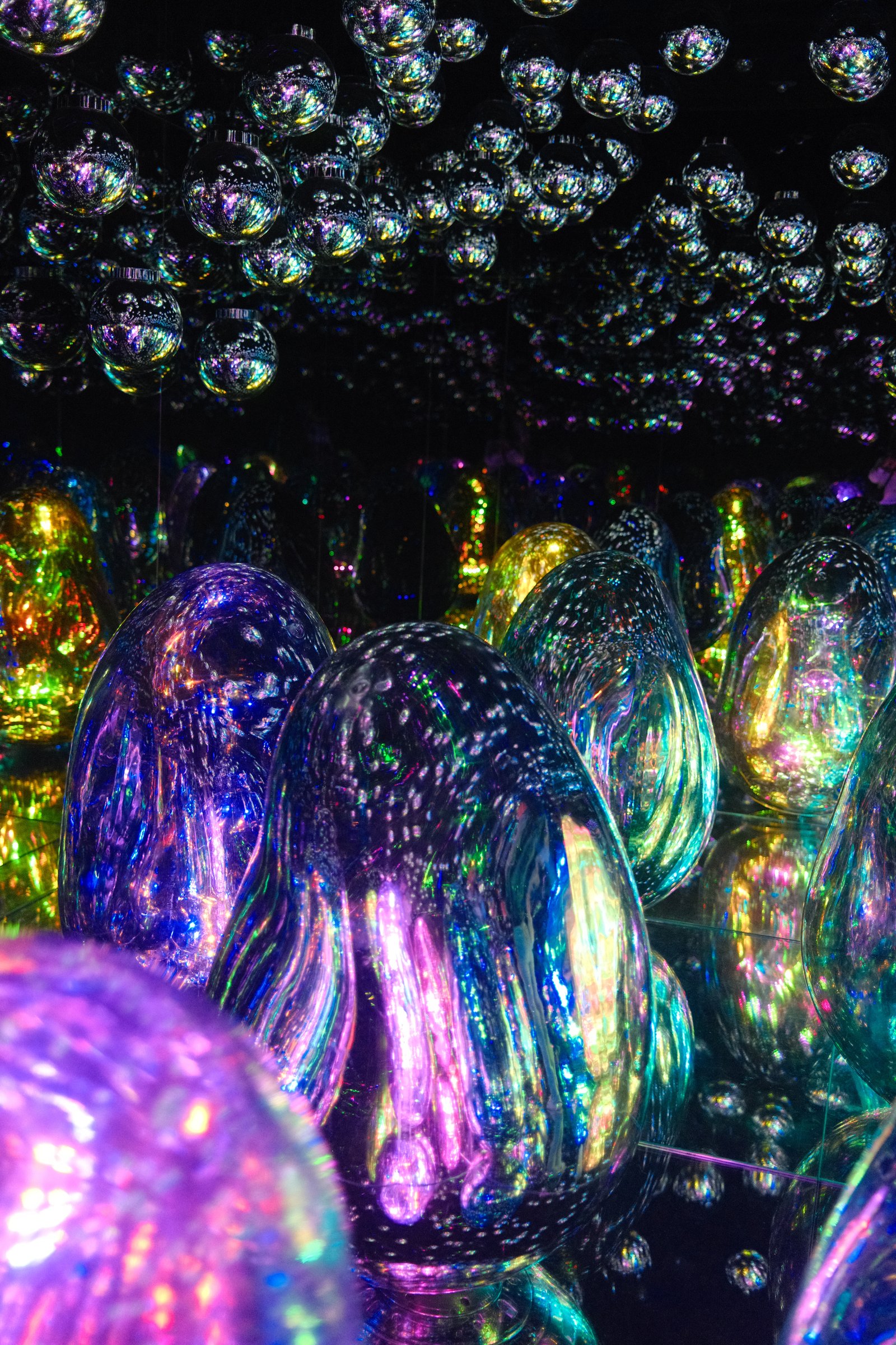 Iridescent, egg-shaped mirrored sculptures at an immersive art installation, with mirror balls suspended overhead.