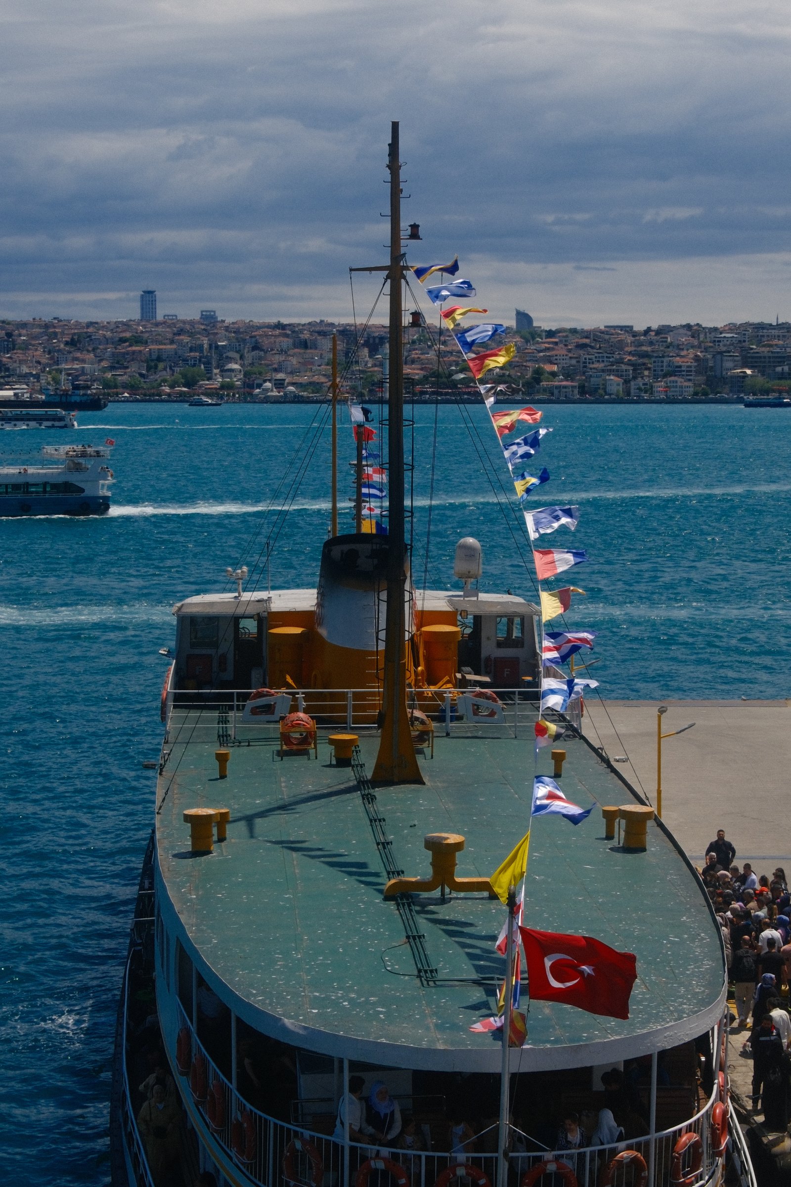 The deck of a heritage ferry strung with signal flags and a Turkish flag, the city skyline behind.